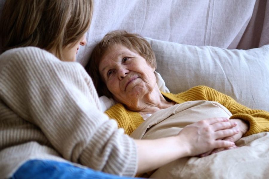 Cuidadora acompañando a una adulta mayor en cama durante su recuperación en casa